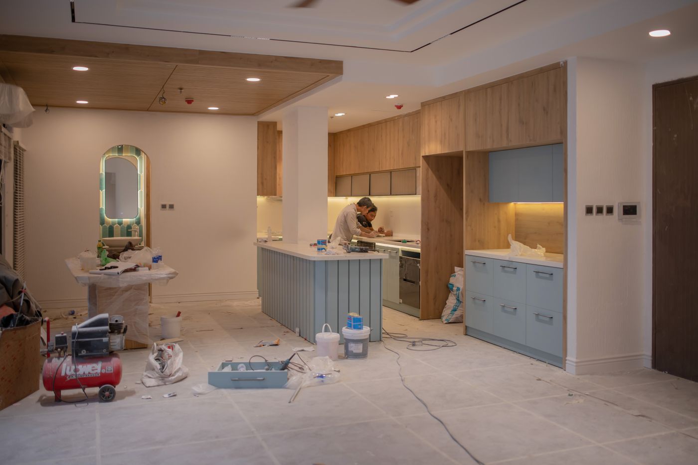 Two workers fitting cabinetry in a kitchen mid-renovation, with tools and dust sheets on the floor