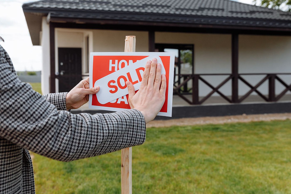 A sold sticker being placed over a home-for-sale sign in front of a finished house