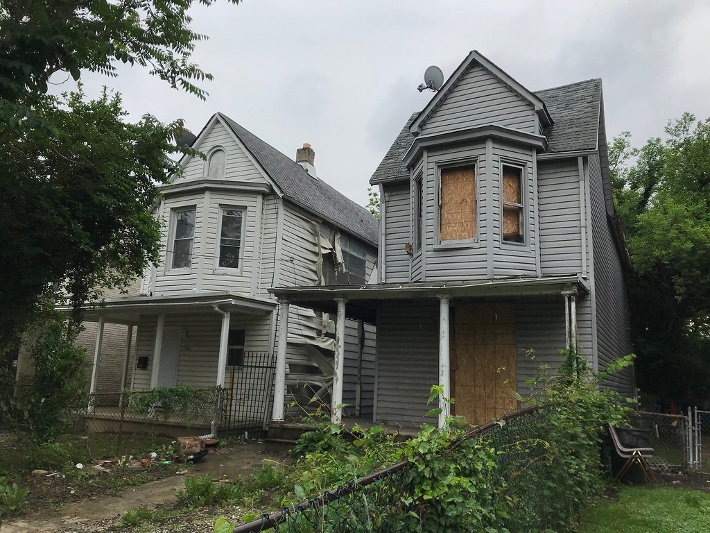 Two vacant wood-frame houses with boarded windows and overgrown front yards
